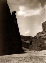 Three Navajos on horseback dwarfed by canyon walls.